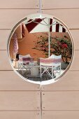 View through porthole in wooden door of wooden terrace with comfortable director's chairs and parasol