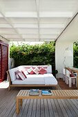 Veranda with comfortable lounger island in front of garden wall covered in lush vegetation