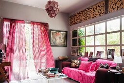 Gemütliches Sofa mit rosé farbenen Kissen und Überwurf vor Sprossenfenster, die geöffnete Terrassentür läd zum Spaziergang in den Garten ein