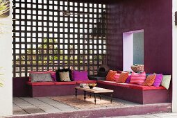 South American terrace area with seat cushions and many scatter cushions on bench and view of garden through wooden lattice wall