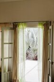 Opened French window with gauzy curtains leading to inviting exotic garden beyond