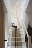 Tree silhouette painted on the wall at the top of a staircase with a runner made from antique linen grain sacks
