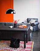 Mit Tafelfarbe lackierter Holztisch auf Webteppich mit farbenfrohem Ethnomuster; dahinter eine gemütliche Sitzgarnitur in Grau