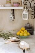 Mother-of-pearl dishes and a ceramic bowl of lemons on a tiled white worktop; lanterns hanging from ornate curved brackets which support the crockery shelf Eastern-style in a kitchen corner