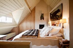 Gemütliches Doppelbett und Jagddekoration in einem Dachgeschoss-Schlafzimmer mit schräger Holzdecke