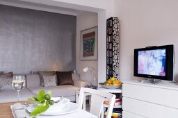 White living room couch in alcove against grey wall; set dining table and TV running in foreground