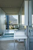 Badezimmer mit eingelassener Badewanne vor großer Spiegelwand; im Spiegel die Reflexion der Landschaft und des Häusermeeres