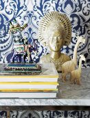 Animal figurines and gilt bust on marble shelf against blue and white patterned wallpaper