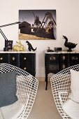 White, bertoia wire chairs in front of a extravagant, black, English style chests of drawers