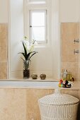 Renovated bathroom with pale stone tiles on wall and bathtub and orchid in window niche