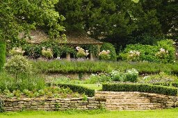 Terrassierter Garten in Sommerstimmung mit formgeschnittenen Hecken an Treppe und niedrige Mauern aus Naturstein