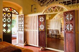 Bedroom with open terrace door; wooden partition wall with carved arch and open double doors showing view of adjacent room