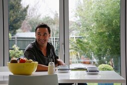 Mann beim Nachmittagskaffee an modernem Esstisch vor Terrassenfenster