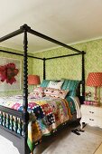 Schwarzes Himmelbett mit buntem Patchwork-Überwurf in grün gemustertem Zimmer; neben dem Bett Nachttischlampen mit rot gemustertem Stofflampenschirm