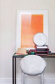 White plastic shell chair at desk with modern artwork leaning on wall