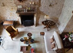 Top view of rustic living room with exposed stone walls and lounge area in front of open fireplace