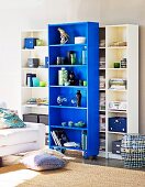 Shelving units with blue element on castors and cushions on floor in front of partially visible sofa
