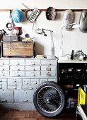 Rad vom Motorrad vor Vintage Schubladenschrank und aufgehängte Blechteile an Wand