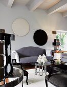 Grey, curved sofa against wall with circular artworks and glass-topped coffee table in living room with wood-beamed ceiling