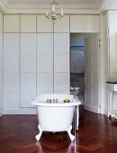 Free-standing vintage bathtub on high-quality, dark wood herringbone floor and coffered wooden partition in white bathroom