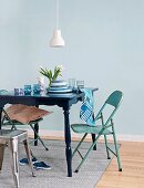 Farblich passende Accessoires auf dunkelblau lackiertem Tisch mit türkisfarbenen Klappstühlen und Metallhocker im industriellen Vintagelook