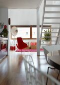 View past white staircase into living room with red designer armchair and designer standard lamp