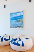 White and blue beanbags on pale wooden floor below seascape painting