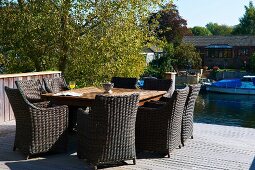Sunny, wooden deck on river bank with wicker chairs and square table