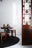 Chinese-style screen next to round tea table set with tea service on black rug