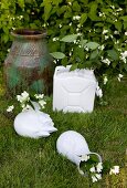 weiße Vasen und ehemaliger Kanister mit Jasmin Blumenzweigen neben Bodenvase im Garten