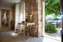 Delicate, old metal table against rustic stone wall and view of garden through open door