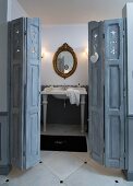 Antique sink below oval, gilt-framed mirror; grey, folding panelled door in foreground