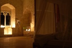 Unique ambiance in candle-lit bedroom in Chateau Maignaut with canopied bed and ancient masonry