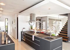 Free standing, gray kitchen counter unit beneath a suspended ceiling in a modern, open living room across from a stairway
