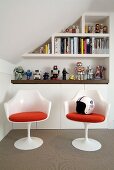 White plastic shell chairs with red cushions in front of sideboard and shelving on wall of attic room