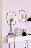Tour Eiffel made of wire on a white sideboard next to a Chinese vase; picture frames with flower pictures drawn on the wall