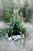Christmas tree decorated with baubles, garlands and wrapped presents in woodland clearing
