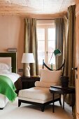 Eleganter weißer Polstersessel in Schlafzimmerecke vor olivgrünen Vorhängen mit Beistelltischchen und Designertischleuchte
