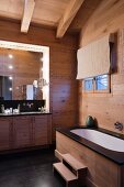 Chalet bathroom - wood-clad bathtub with steps opposite washstand with base cabinets and illuminated mirror