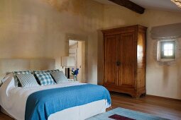 Double bed with blue and white bed linen and rustic wooden wardrobe within historical walls of Proven
