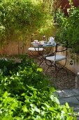 Lauschiges Plätzchen in mediterranem Garten mit schmiedeeisernen Stühlen, gedeckt für zwei zur Kaffeezeit