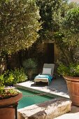 Sun lounger on wooden deck next to pool surrounded by Mediterranean plants