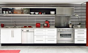 Moderne weiße Küchenzeile mit schwarz-weiß gestreifter Rückwand und seitlichem Wandspiegel und roten Küchengeräten