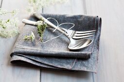 Cutlery and heart made from wire and herbs on napkin