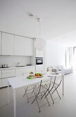 White, designer interior with dining table and folding chairs in front of open-plan kitchen