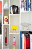 Weisses Bücherregal mit Büchern, Kunstobjekten und Modellen von Designerstühlen
