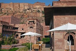 Aussenansicht mit Sonnenschirmen, Restauranttischen und Gartenanlage vom Hotel Raas Haveli, Jodhpur, Indien, mit Ausblick auf die Bergfestung