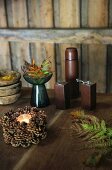 Kleiner Kranz aus Kiefernzapfen, Farnblätter und Salzstreuer und Pfeffermühle auf einem rustikalen Holztisch
