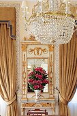 Chandelier in front of gilt console table with mirror flanked by gathered curtains