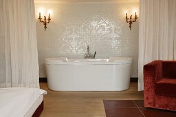 En suite bathroom separated by curtain with modern free-standing bathtub below antique sconces (Schloss Schauenstein)
